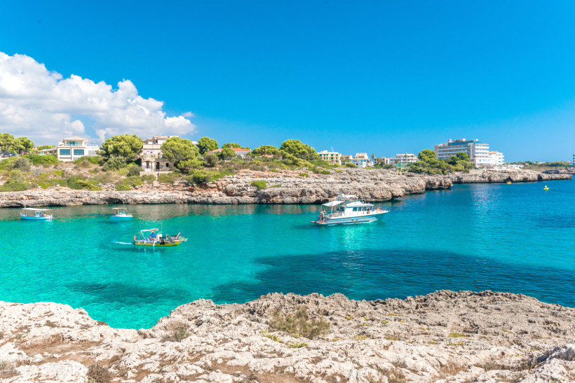 Boote in der Bucht von Cala Marcal bei Portocolom mit felsiger Küste und türkisblauem Wasser