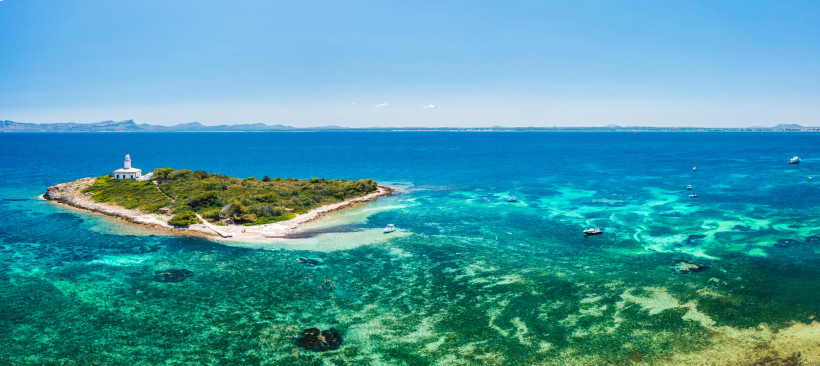 Luftaufnahme der vorgelagerten Insel Alcanada mit Leuchtturm, flachem Wasser, Fels- und Sandbereichen sowie Booten vor der Nordküste Mallorcas