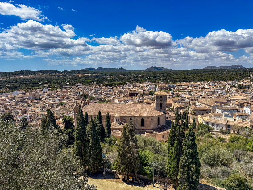 Blick über die historische Altstadt von Artà auf Mallorca mit Kirche, Naturstein-Häusern und grüner Hügellandschaft im Hintergrund