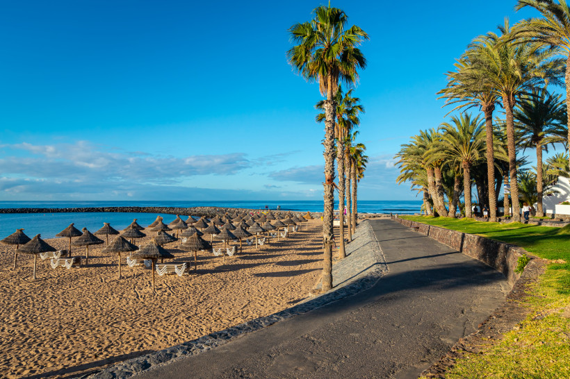 Strand von Playa de las Américas auf Teneriffa mit Palmenpromenade, Sonnenschirmen und goldenem Sand