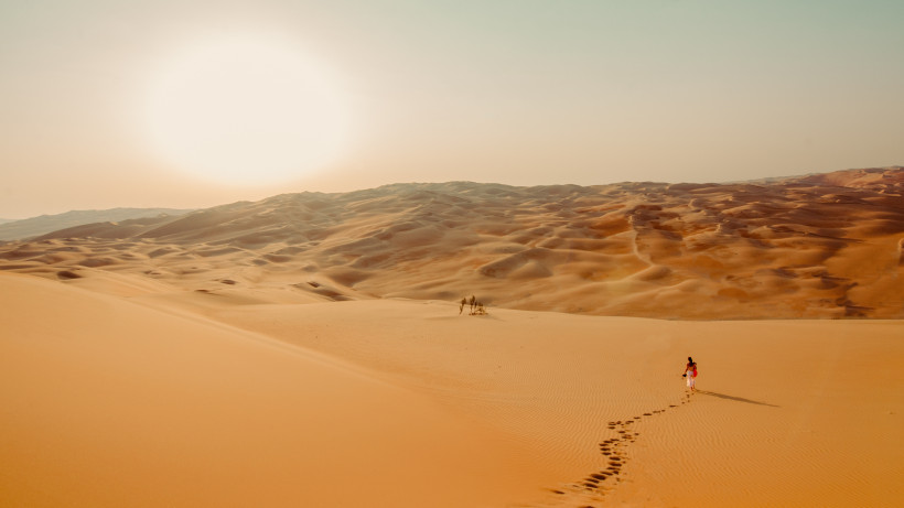 Dünenlandschaft in den Vereinigten Arabischen Emiraten bei tief stehender Sonne, Person mit Fußspuren im Sand