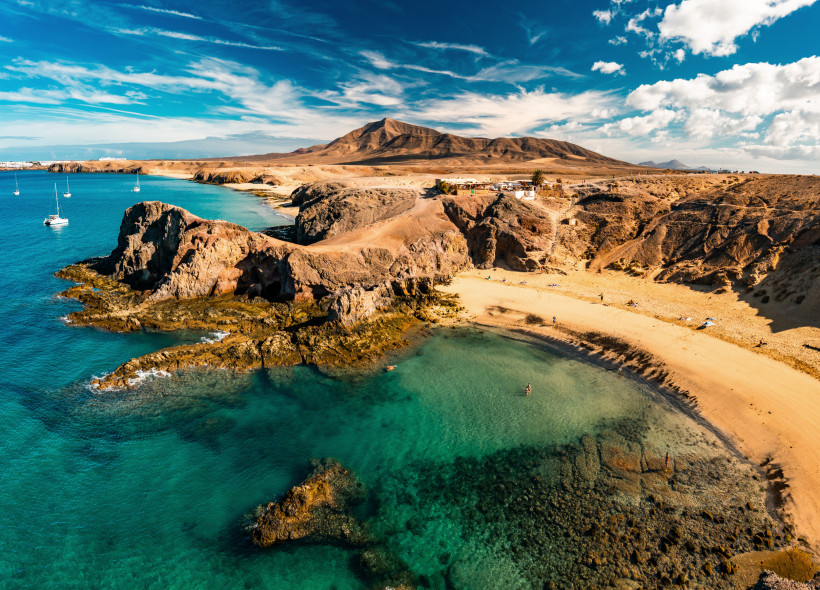 Papagayo-Strände: Sandbucht und Felsenküste an türkisfarbenem Meer Blick über die Papagayo-Strände mit Felsenküste, Sandbuchten und türkisfarbenem Meer, im Hintergrund karge Hügellandschaft und Segelboote