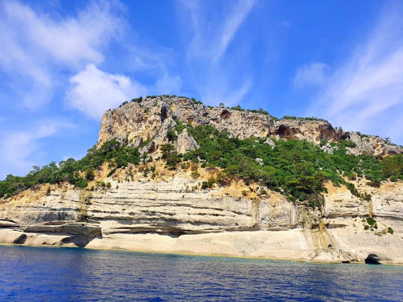 Felsenküste bei der Beldibi-Höhle an der Türkischen Riviera mit steiler Klippe, grüner Vegetation und tiefblauem Mittelmeer