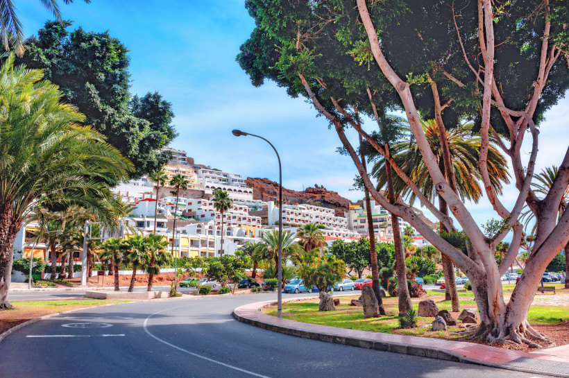 Straße mit Palmen und Parkanlage in Puerto Rico auf Gran Canaria, im Hintergrund weiße Hotelanlagen am Hang