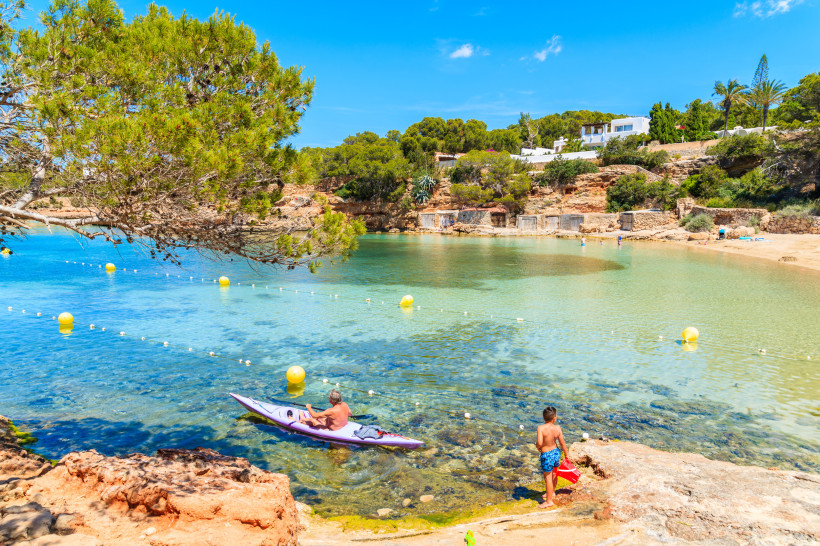 Bucht bei Sant Antoni mit Kajak im flachen Wasser, Badebereich mit Bojen und Felsufer