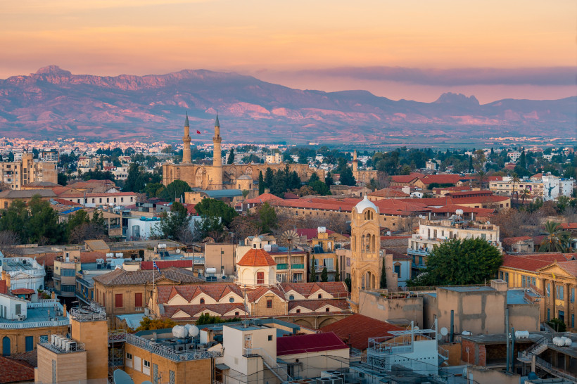 Panoramablick auf Nikosia (Lefkosia) bei Sonnenuntergang mit Stadt­dächern, Minaretten und dem Kyrenia-Gebirge im Hintergrund.