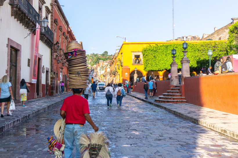 Straßenszene in San Miguel de Allende, Mexiko: Straßenverkäufer mit Hüten und bunten Häuserfassaden – Kolonialstadt 