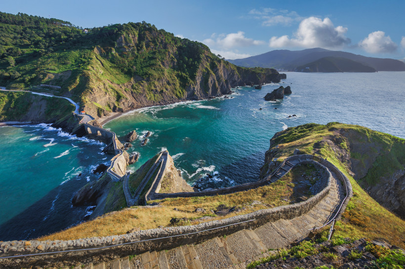 Küstenlandschaft bei San Juan de Gaztelugatxe mit Serpentinenweg und Steintreppe über einer türkisfarbenen Bucht