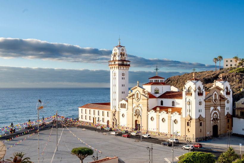 Basilika Nuestra Señora de Candelaria am Meer auf Teneriffa Basilika Nuestra Señora de Candelaria auf Teneriffa mit hellen Fassaden und markantem Glockenturm direkt am Atlantik, umgeben von Festplatz und Hügeln, unter blauem Himmel mit Wolken.