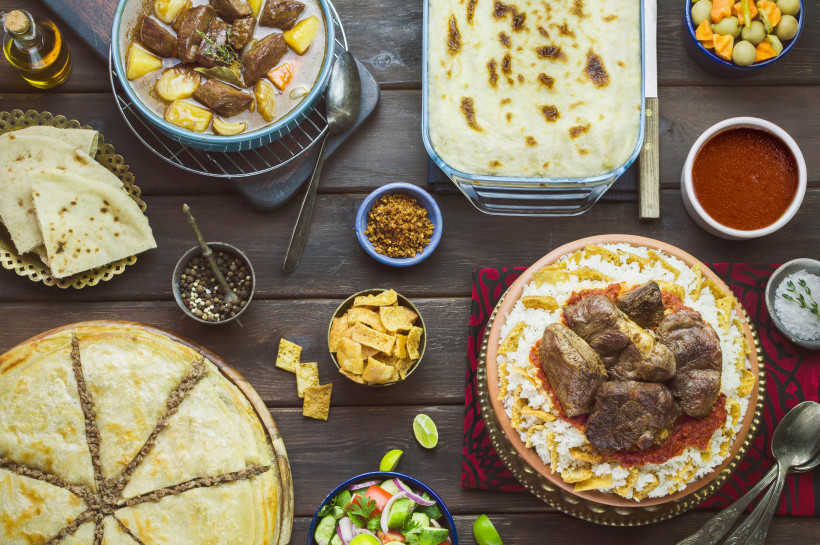 Ägypten - Makadi Bay Orientalische Festtafel mit Lammfleisch auf Reis, Fladenbrot, Auflauf, Eintopf, Gemüse, Salat und Gewürzen auf einem Holztisch. Die Speisen sind vielfältig und farbenfroh angerichtet.