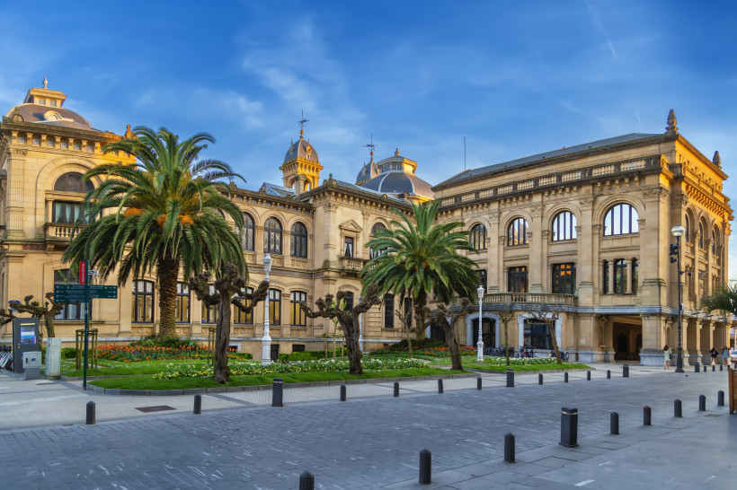 Das prächtige Rathaus von San Sebastián mit klassizistischer Architektur, Palmen und gepflegtem Blumenbeet im Vordergrund.