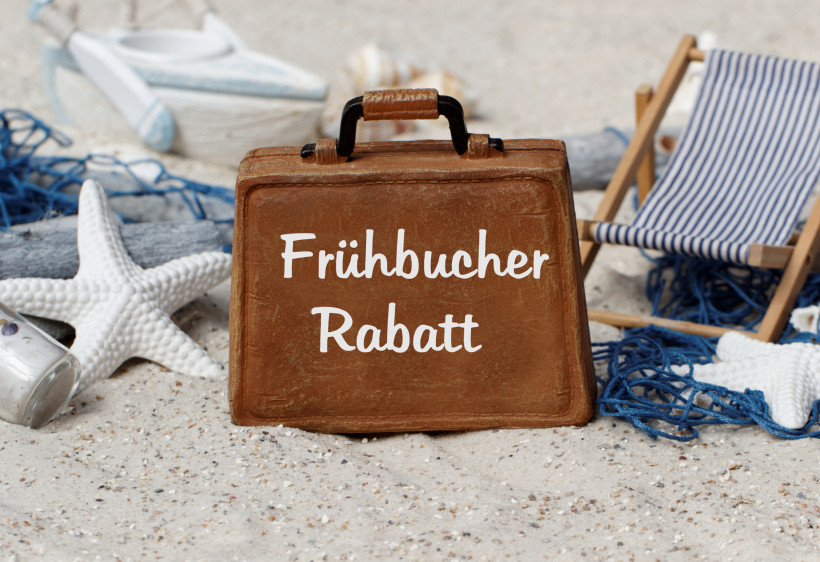 Dekoratives Strandmotiv mit kleinem Koffer, der den Schriftzug 'Frühbucher Rabatt' trägt, umgeben von Liegestuhl, Sternen und maritimen Accessoires
