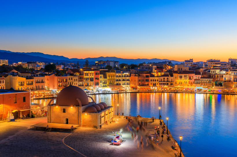 Abendansicht des Hafens von Chania mit beleuchteten Gebäuden und Uferpromenade Chania Hafen in der Dämmerung mit beleuchteter Uferpromenade, Wasserbecken und Kuppelgebäude im Vordergrund