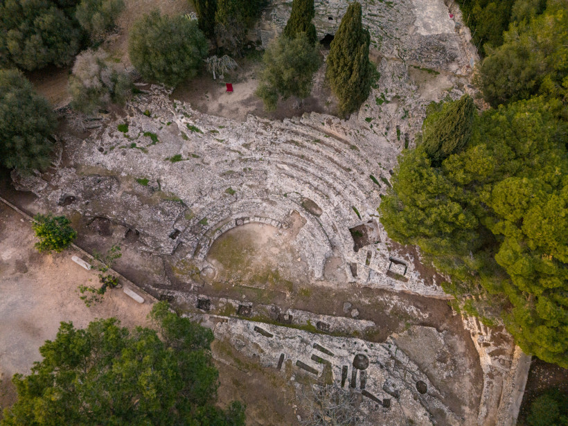 Luftaufnahme des römischen Theaters von Pollentia nahe Alcúdia mit halbkreisförmigen Steinstufen und umgebender mediterraner Vegetation.