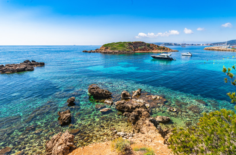 Blick auf die Bucht von Puerto Portals mit felsiger Küste, klarem türkisfarbenem Wasser und Booten vor einer kleinen Insel