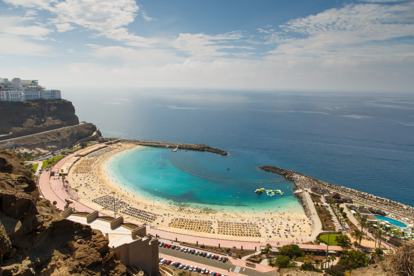 Playa de Amadores – Beliebter Strand auf Gran Canaria,Playa de Amadores – Gran Canaria Blick auf die halbkreisförmige Playa de Amadores mit ruhigem türkisfarbenem Wasser, Liegestuhlreihen, Promenade, Wellenbrechern und Wasserspielplatz auf Gran Canaria