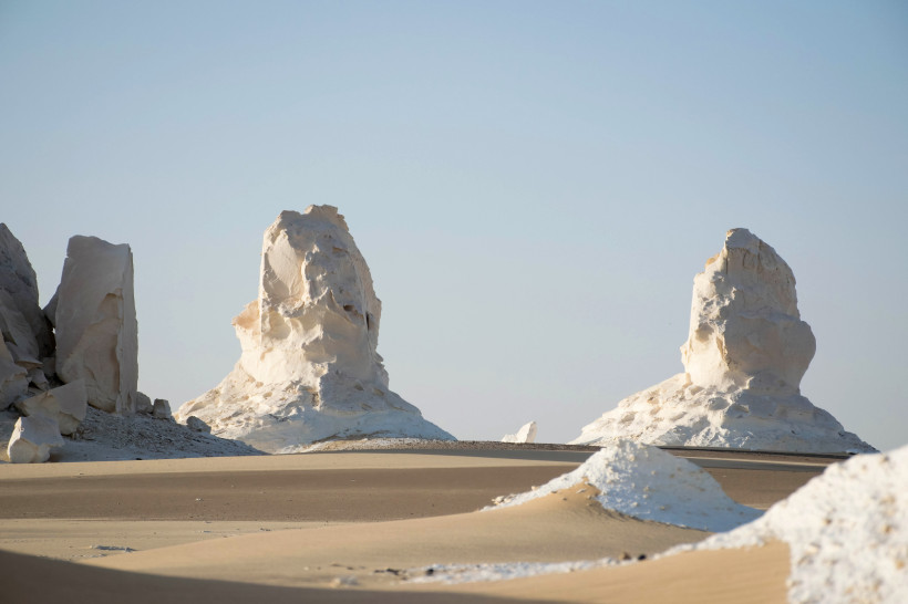 Das Bild zeigt zwei auffällig geformte, helle Kalksteinfelsen in der Weißen Wüste Ägyptens. Die Formationen erinnern durch ihre runden, schmal zulaufenden Silhouetten an Pilze oder abstrakte Skulpturen. Der Boden ist eine Mischung aus feinem, beigem Wüste