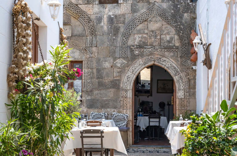 Traditionelles Restaurant in der Altstadt von Rhodos mit Steinbogen, gedeckten Tischen und mediterraner Begrünung