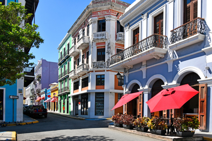 Straßenszene in der Altstadt von San Juan mit bunten Kolonialgebäuden, Balkonen und roten Sonnenschirmen