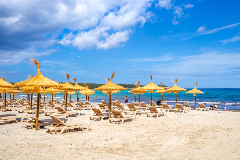 Strand von Sa Coma mit Strohschirmen und Liegen am Sandstrand, im Hintergrund das Meer