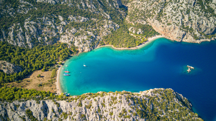 Bootstour Belek – Traumhafte Küstenlandschaft und türkisfarbene Badebuchten entdecken Luftaufnahme einer idyllischen Bucht mit türkisfarbenem Wasser und Ausflugsbooten entlang der Küste von Belek in der Türkei.