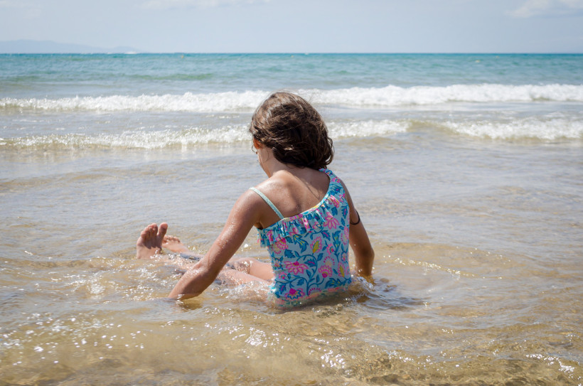 Kind sitzt im flachen Wasser am Familienstrand von Kokkini Hani, im Hintergrund das Meer mit kleinen Wellen.
