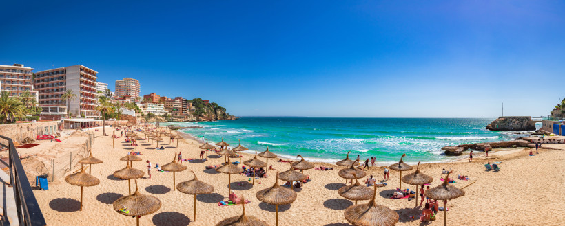 Strand von Cala Major mit Strohschirmen, Badegästen und türkisfarbenem Meer