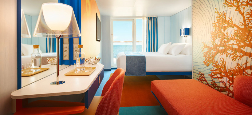 Balkonkabine auf der Costa Toscana mit Doppelbett, Sitzbereich und Blick aufs Meer durch die Balkontür