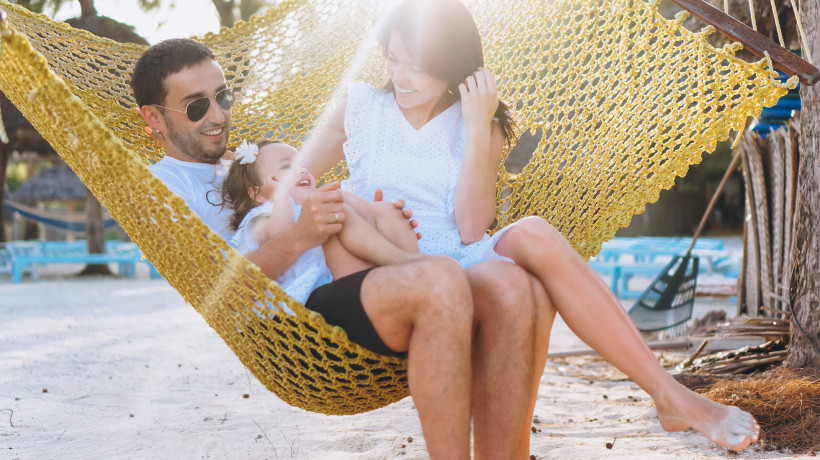 Familie am Strand in Hängematte, 2 Erwachsene und 1 Kinde bei Sonnenschein