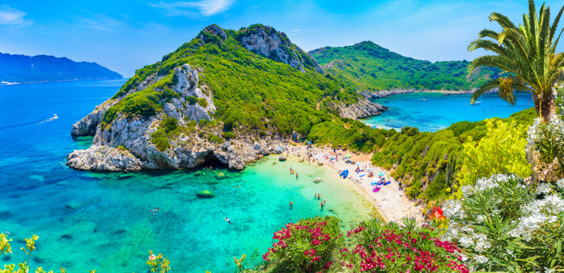 Bucht mit türkisfarbenem Meer, Kiesstrand und grünen Hügeln auf Korfu