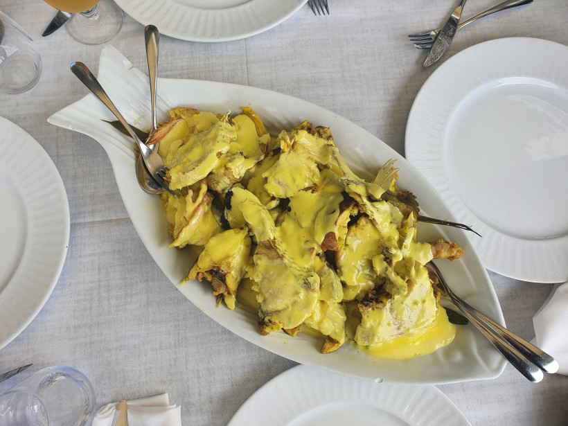 Bullit de Peix auf einer Servierplatte mit gelber Sauce Servierplatte mit Bullit de Peix, Fischstücken mit gelber Sauce auf einem gedeckten Tisch
