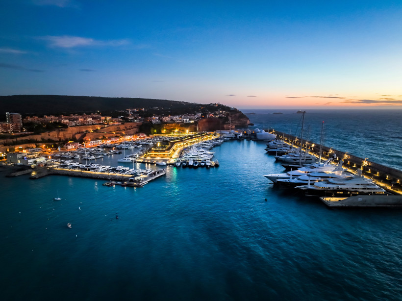 Port Adriano Marina bei Dämmerung mit beleuchteten Stegen und Yachten am Hafenbecken