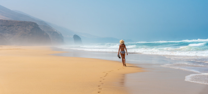 Playa de Cofete auf Fuerteventura – Einsamer Traumstrand mit beeindruckenden Klippen Frau spaziert am endlosen, naturbelassenen Strand der Playa de Cofete auf Fuerteventura mit Blick auf die mächtigen Klippen.