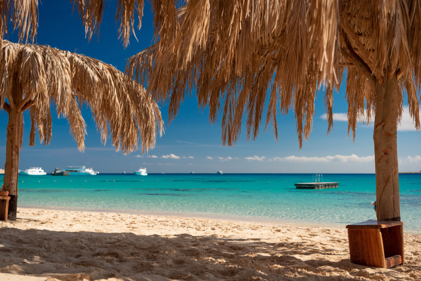 Tropischer Strand mit Schatten spendenden Palmendächern und türkisblauem Meer