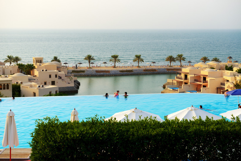 Ras al Khaimah, Winter Infinity-Pool mit Blick auf ein luxuriöses Resort, Palmen, Sandstrand und das Meer im Hintergrund