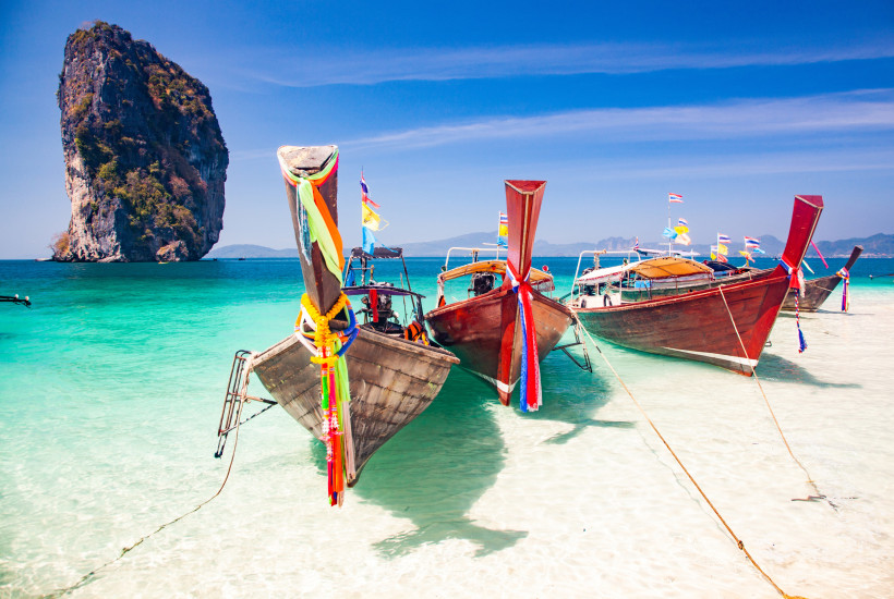Longtail-Boote am Strand von Poda Island bei Krabi in Thailand mit türkisblauem Meer und Kalksteinfelsen.