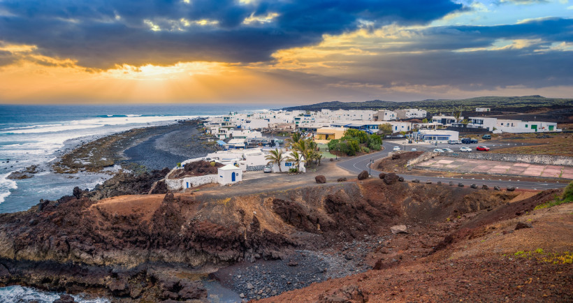 Blick auf das Fischerdorf El Golfo auf Lanzarote mit weißen Häusern, schwarzer Lavaküste und Sonnenuntergang über dem Atlantik.