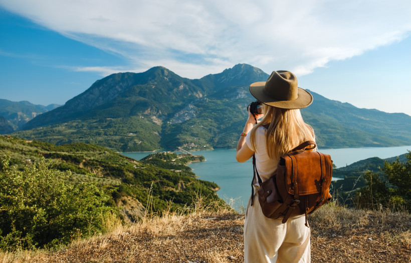 Wandern, Griechenland Frau mit großem Rucksack macht Fotos von Bergen und blauem See.