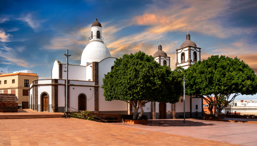 Historische Kirche auf Gran Canaria – Sonnenuntergang über dem Stadtplatz Historische Kirche auf Gran Canaria bei Sonnenuntergang – weiße Fassade mit Kuppel, Glockentürmen und Stadtplatz mit Terrakottafliesen.