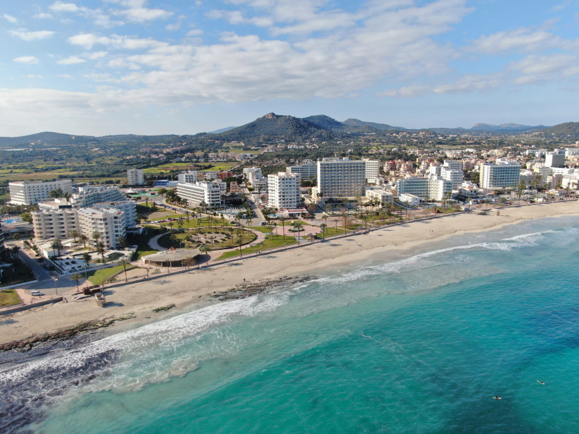Panorama-Luftaufnahme von Cala Millor mit breitem Sandstrand, Hotelanlagen, türkisfarbenem Wasser und grünen Hügeln im Hinterland von Mallorca.