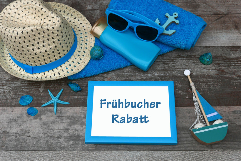 Frühbucher Rabatt – Sommerdeko mit Sonnenhut, Sonnenbrille und Urlaubsaccessoires Sommerliche Strand- und Urlaubsdko mit Sonnenhut, blauer Sonnenbrille, Handtuch und Schild „Frühbucher Rabatt“ als Motiv für günstige Frühbucherangebote.