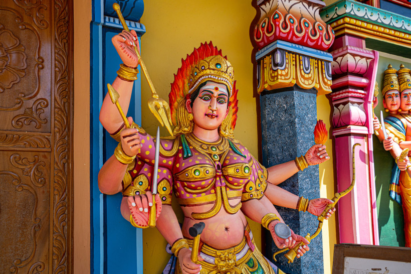 Dieses Bild zeigt eine beeindruckende, farbenfrohe Statue einer hinduistischen Göttin, vermutlich Durga oder Kali, die für Schutz und göttliche Macht steht. Die Figur hat mehrere Arme, von denen jeder ein Symbol oder eine Waffe hält, darunter ein Schwert,