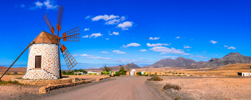 Traditionelle Windmühle auf Fuerteventura vor Bergen und blauem Himmel