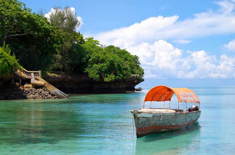 Sansibar - Chumbe Island Traditionelles Holzboot mit orangefarbenem Sonnendach im türkisfarbenen Wasser vor der grünen Küste von Sansibar, Tansania