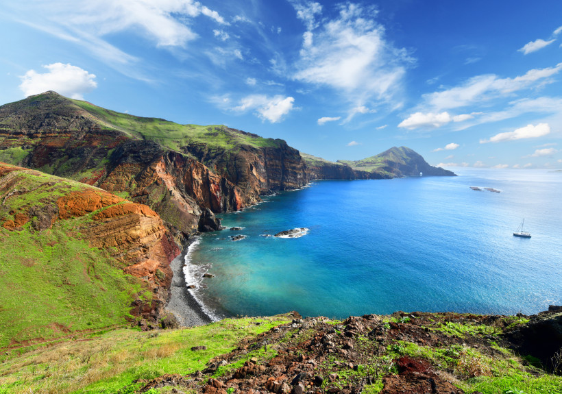 Steilküste und Bucht auf Madeira unter blauem Himmel Küstenlandschaft auf Madeira mit steilen Felsen, grünen Hängen und blauer Bucht