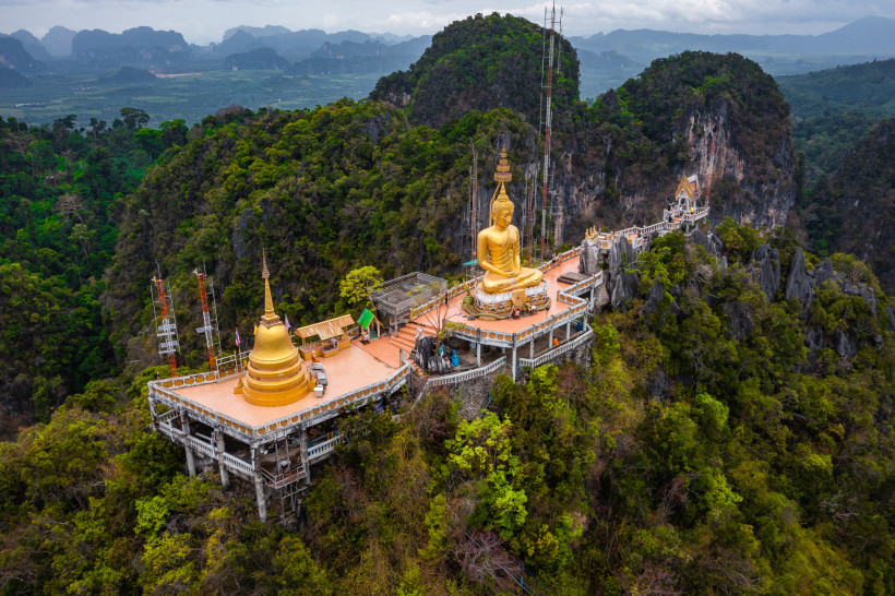 Thailand - Krabi Das Bild zeigt eine Luftaufnahme des Tiger Cave Temple (Wat Tham Sua) bei Krabi, Thailand. Im Zentrum der Szene thront eine große, goldene Buddha-Statue in Meditationshaltung auf einem Tempelplateau, das hoch oben auf einem Kalksteinfelsen erbaut wurde. D