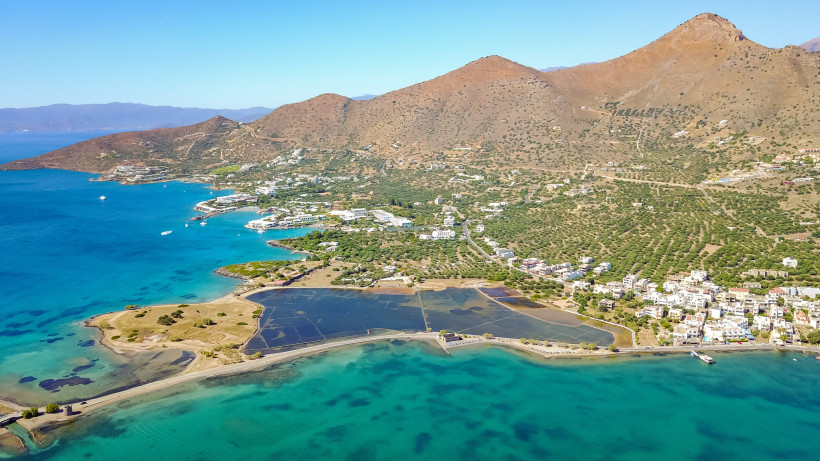 Luftaufnahme der Küste bei Elounda mit türkisfarbenem Meer, Lagune, Siedlung und Bergen im Hintergrund