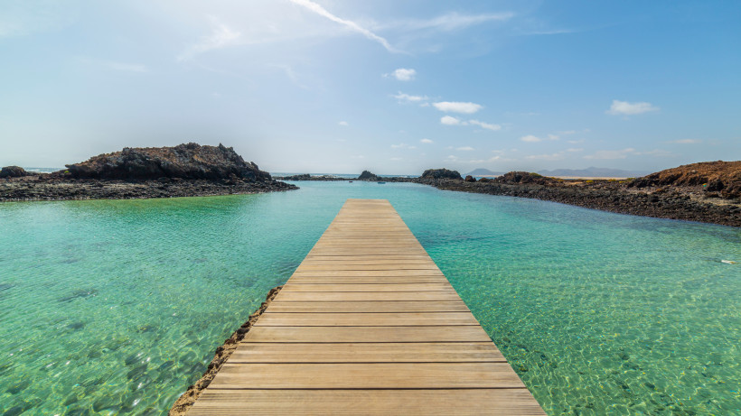 Holzsteg über türkisfarbenem Wasser zwischen dunklen Felsen auf der Insel Lobos