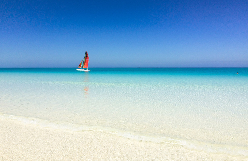 Segelboot mit bunten Segeln auf dem kristallklaren türkisfarbenen Meer am Strand von Cayo Guillermo auf Kuba – Karibikfeeling pur bei strahlend blauem Himmel.