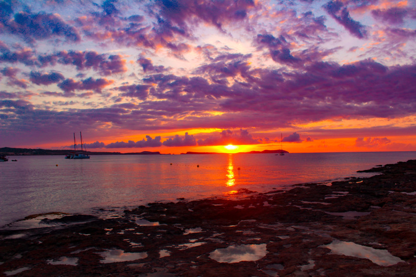 Sonnenuntergang über dem Meer bei Café Mambo mit Segelbooten und felsiger Küste im Vordergrund